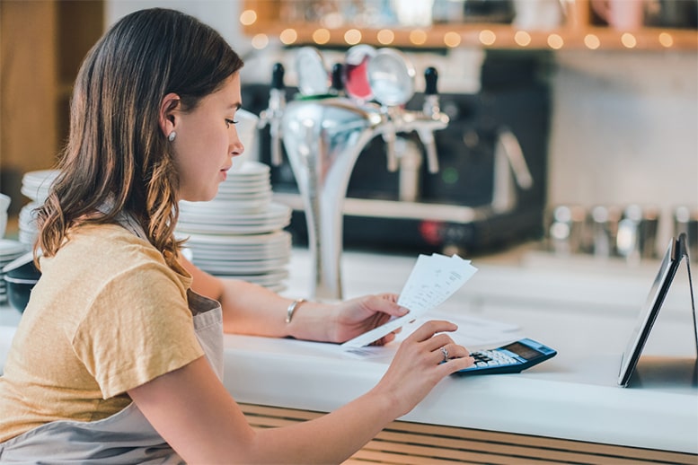 small-business-expense-tracking_375x250 A picture of a young female business owner using a digital tablet and calculator while reviewing paperwork.